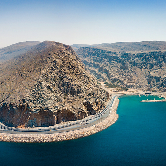 Weitläufiges Wasser mit einer Strasse, die über die Wasseroberfläche im Musandham, Oman, verläuft.