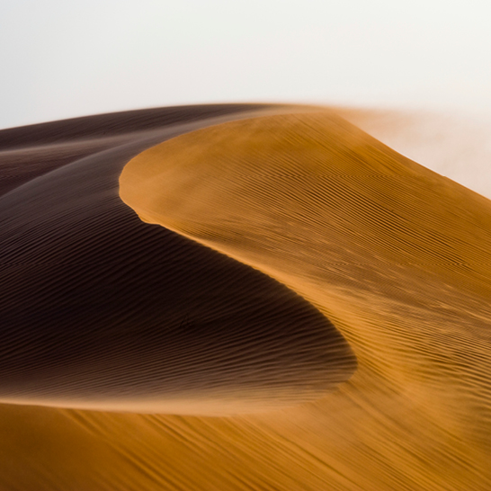 Eine Person geht über eine Sanddüne in den Sharqia Sands, Oman, umgeben von goldenem Sand und klarem Himmel.