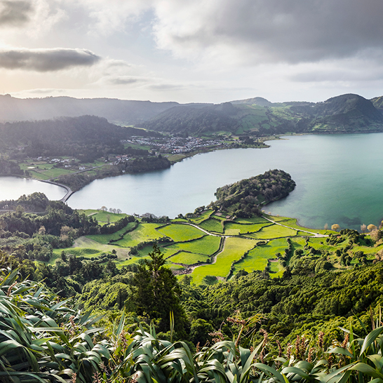 Malerische Aussicht auf einen See, umgeben von sanften Hügeln und einem kleinen Dorf.