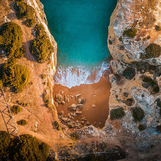 Luftaufnahme eines Strandes mit einer Klippe im Hintergrund, die das blaue Wasser und den Sand zeigt.