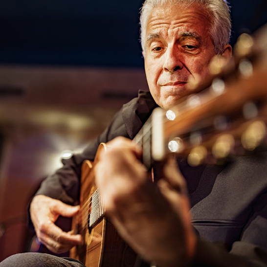 Ein älterer Mann mit weißen Haaren spielt leidenschaftlich auf seiner akustischen Gitarre.