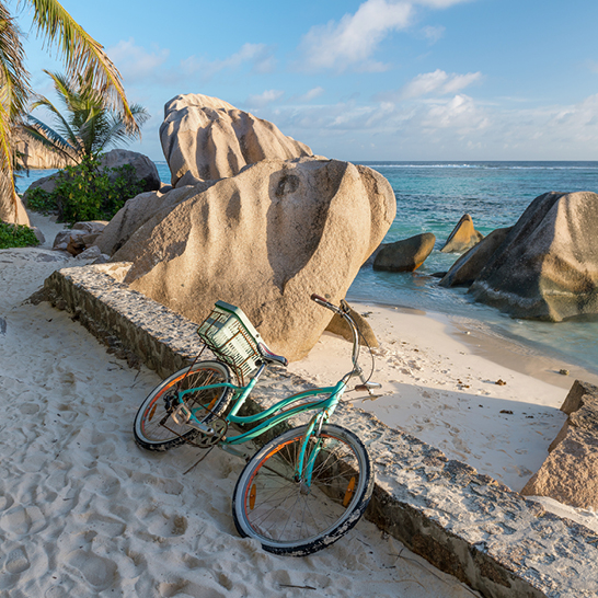 Un vélo stationné sur la plage des Seychelles, près d'un gros rocher.