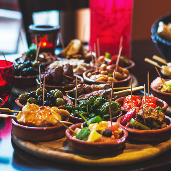 Ein Tisch mit verschiedenen Tapas-Gerichten aus Spanien, darunter Oliven, Käse und kleine Häppchen.