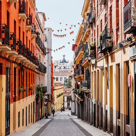 Enge Strasse in Madrid mit zahlreichen Gebäuden und Balkonen, die eine lebendige städtische Atmosphäre schaffen.
