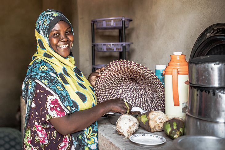 Eine lächelnde Frau hält einen Korb mit Lebensmitteln, umgeben von der Kultur Tansanias.