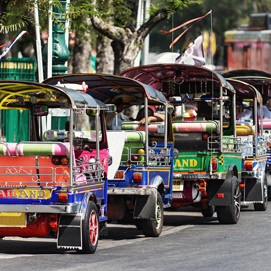 Un groupe de tuk-tuks colorés garés sur une rue animée en Thaïlande.