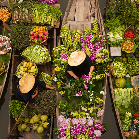 Une femme dans un bateau rempli de légumes, naviguant sur une rivière en Thaïlande.