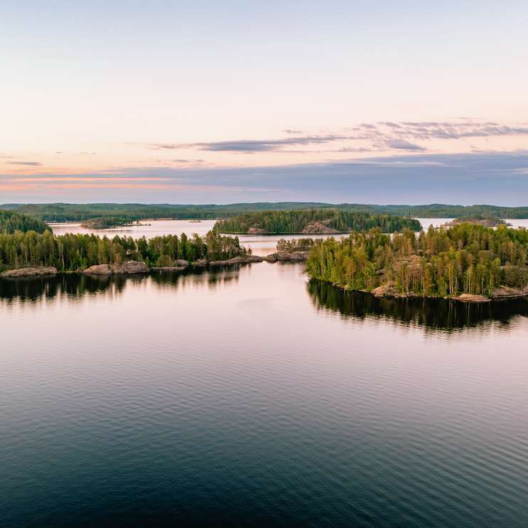Vue aérienne d'un lac entouré d'arbres en Finlande, offrant un paysage naturel paisible et verdoyant.