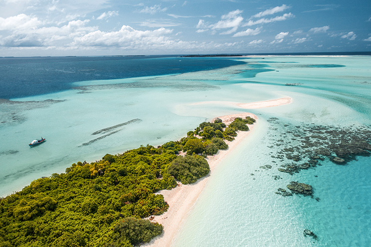Luftaufnahme einer tropischen Insel auf den Malediven mit weissem Sand und blauem Wasser.