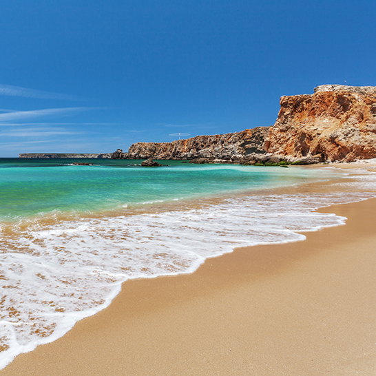 Ein Strand in Sagres mit einer Welle, die sanft an die Küste rollt.