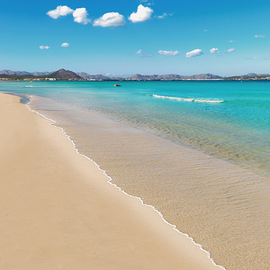 Sandstrand in Can Picafort, Mallorca, mit feinem, goldenem Sand und sanften Wellen im Hintergrund.